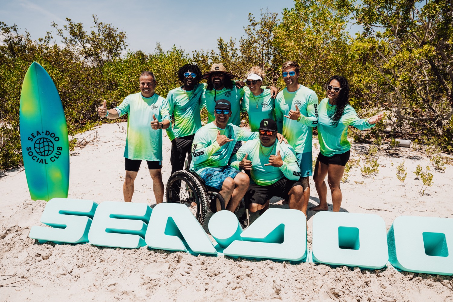 Sea-Doo Social Club crew posing at the giant SEA-DOO sand letters with a branded surfboard